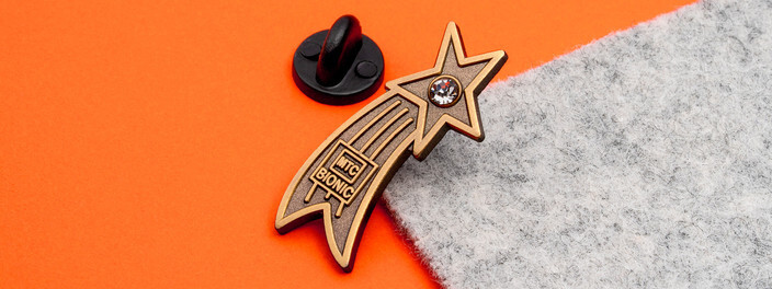 Gold shooting star pin with a clear crystal at its point, beside a black clutch on orange paper and gray felt