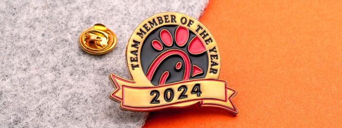 Gold Team Member of the Year 2024 pin with a red logo over a ribbon banner, beside a gold clutch
