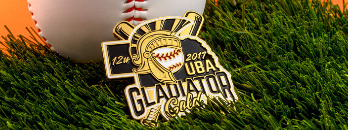Black and gold UBA Gladiator Gold 12u 2017 trading pin with a helmeted gladiator over a baseball, on turf beside a baseball