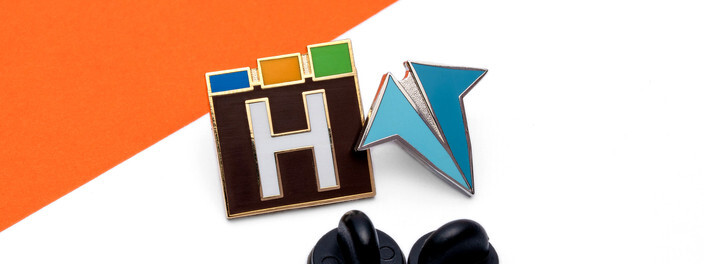 Black and white H logo pin with red, green and blue blocks, beside a teal pin and two black clutches