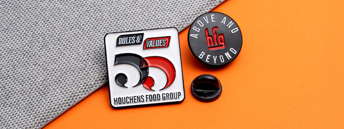 Rules and Values pin beside a round blue Above and Beyond pin, on gray fabric and orange paper