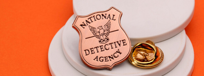 Copper shield pin reading National Detective Agency around an eagle, beside a gold clutch