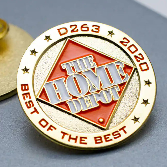 Round gold pin with an orange diamond logo, stars and the words Best of the Best in red, on a gray surface