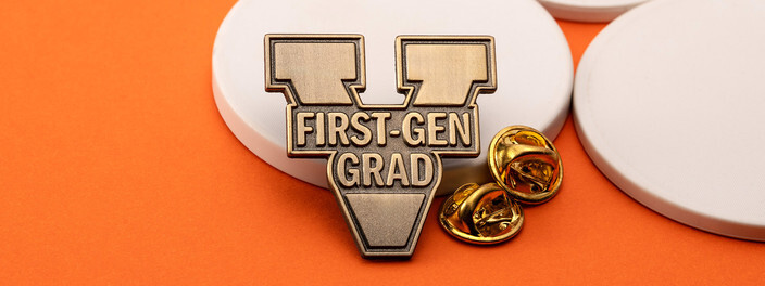 Antique bronze V shaped pin reading First-Gen Grad, beside two gold clutches