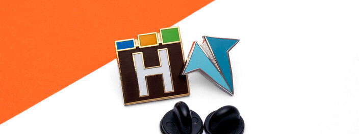 Black and white H logo pin with red, green and blue blocks, beside a teal pin and two black clutches