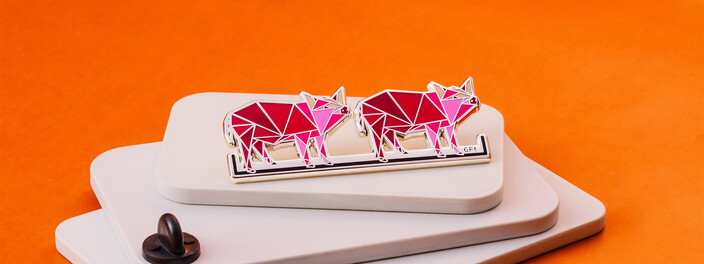 Pin of two pink geometric pigs on a white bar, standing on stacked white tiles over orange paper