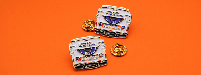 Two ambulance shaped Jersey City Medical Center pins with gold clutches on orange paper
