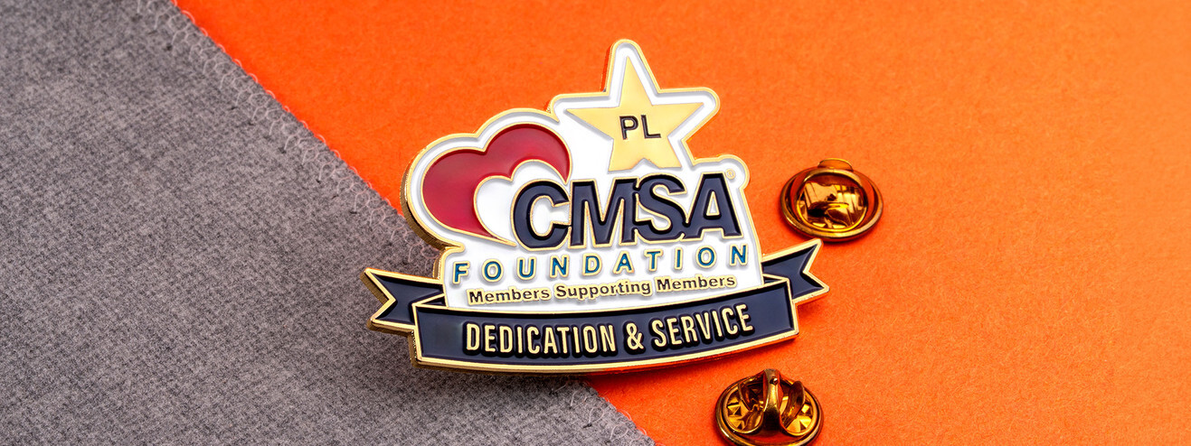 Foundation pin with a red heart, a gold star and a Dedication and Service banner, beside two gold clutches on gray fabric