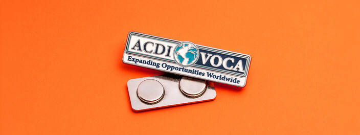 Rectangular name bar pin with a globe and Expanding Opportunities Worldwide, above its silver magnetic back on orange paper