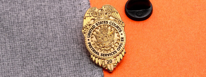 Gold eagle topped pretrial services officer badge pin with the number 20 at the bottom, beside a black clutch