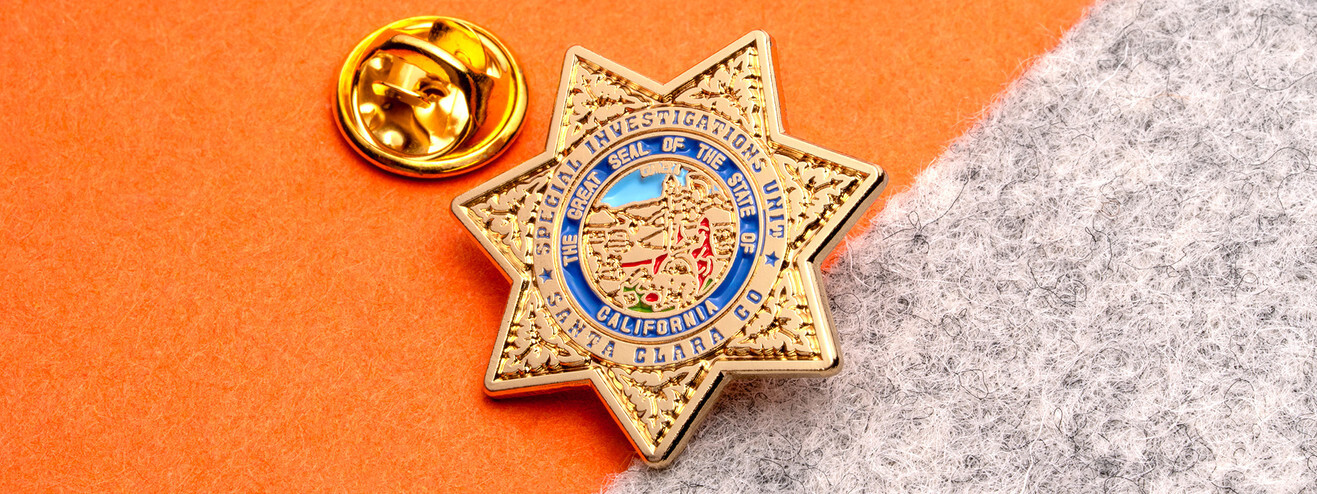 Gold seven point star pin for a special investigations unit with a color state seal in the center, beside a gold clutch