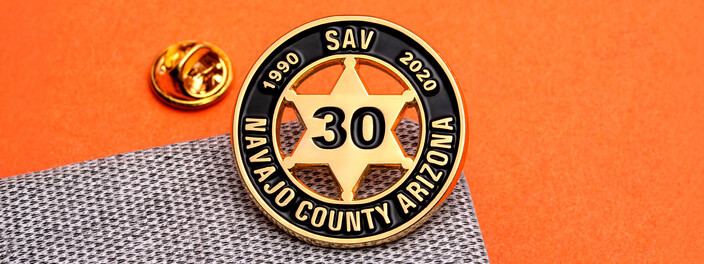 Gold six point sheriff star pin with 30 in the center inside a black ring dated 1990 and 2020, beside a gold clutch