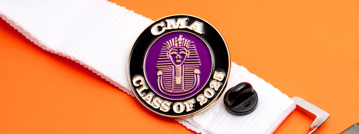 Round black and gold Class of 2025 pin with a purple pharaoh head, pinned to a white lanyard