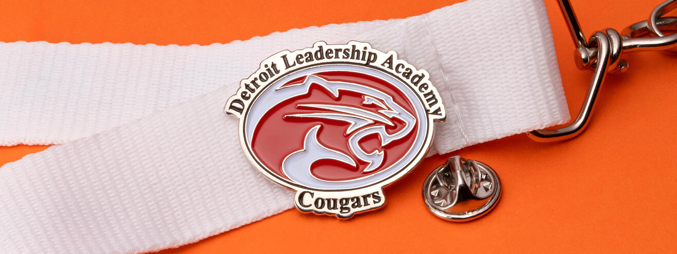 Oval red and white academy pin with a cougar head and the word Cougars, pinned to a white lanyard