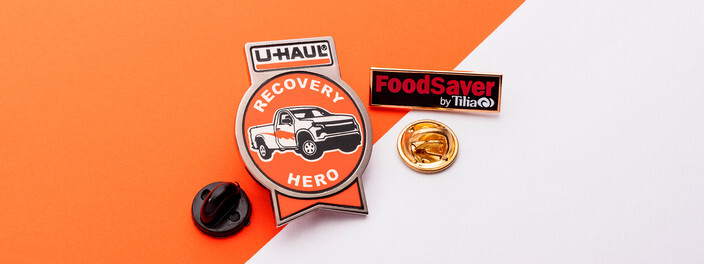 Orange Recovery Hero pin with a pickup truck under a U-Haul tab, beside a red and black FoodSaver bar pin and two clutches