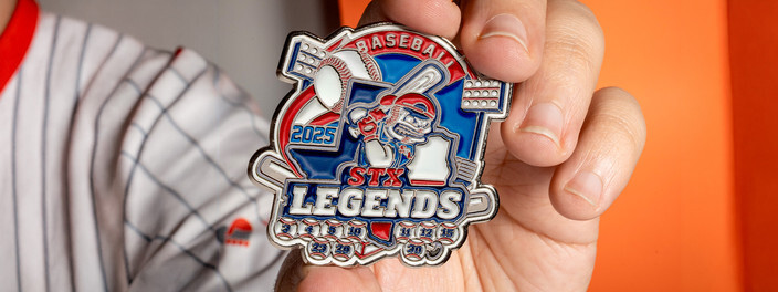 Hand holding a Legends 2025 baseball trading pin with crossed bats, in front of a pinstriped jersey
