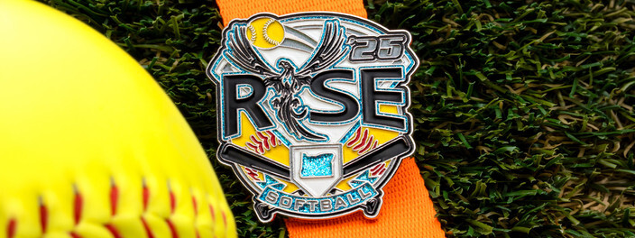 Rise softball trading pin with a phoenix and the number 25, leaning on a yellow softball in the grass