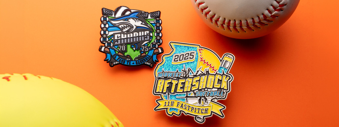 Sharks baseball trading pin and an Aftershock softball pin with a dangler, beside a softball and a baseball on orange paper