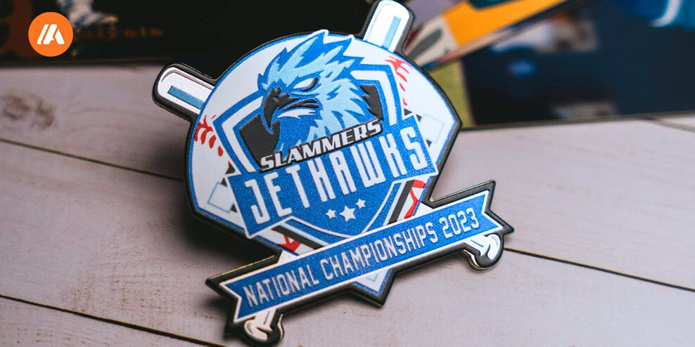 Blue and white hawk baseball trading pin with crossed bats and a National Championships 2023 banner, on white wooden boards