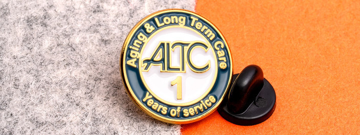 Round navy and white pin with a large gold 1 and Years of Service, beside a black clutch on orange paper and gray felt
