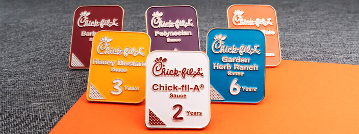 Six rectangular pins shaped like sauce labels in different colors, marked 2, 3 and 6 Years, on gray fabric