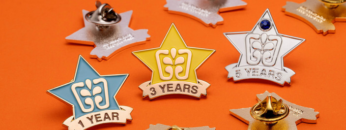 Blue, yellow and silver star pins marked 1 Year, 3 Years and 5 Years, the 5 Years star set with a blue gemstone